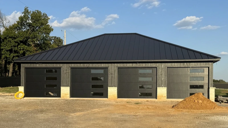 Four black sectional overhead doors installed on a detached garage building