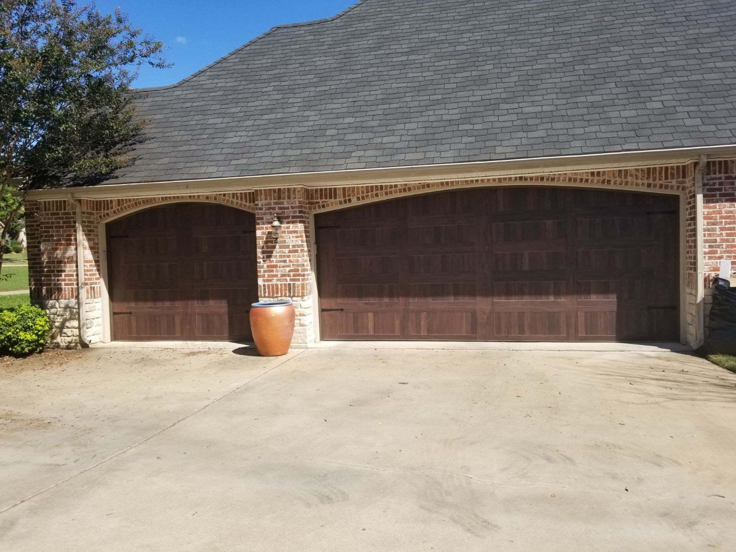 Brown wood-look double and single garage doors installed on a brick home