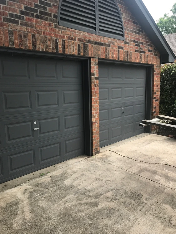 Two dark gray residential garage doors on a brick home